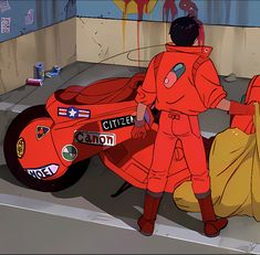 a man standing next to a motorcycle with graffiti on the wall behind it and another person in an orange outfit