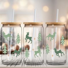 three mason jars decorated with christmas trees and deer silhouettes are on a table in front of a blurry background