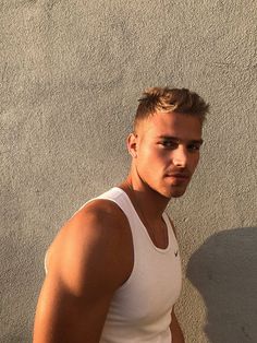 a man in white tank top leaning against a wall