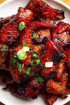 a white plate topped with chicken wings covered in sauce and garnished with green onions