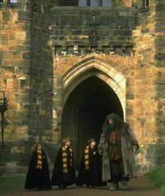 three people dressed in black and yellow robes are standing outside an old castle door with one person wearing a long robe