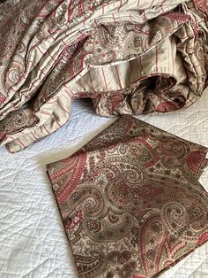 an unmade bed with red and brown paisley bedspread on top of it