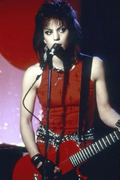 a woman holding a guitar and singing into a microphone