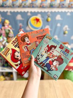 three children's books are held up in front of a wallpapered background