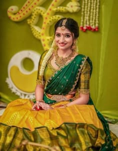 a woman sitting on top of a bed in a green and yellow sari dress