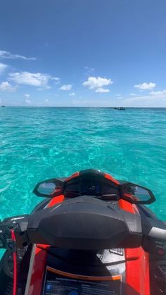 the back end of a red and black jet ski in clear blue water with two people on it