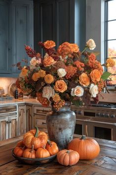 a vase filled with flowers and pumpkins on top of a wooden table in a kitchen