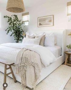 a bed with white linens and pillows in a bedroom next to a potted plant