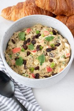 a white bowl filled with food next to croissants