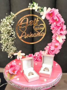 two wedding rings sitting on top of a pink table next to flowers and a sign