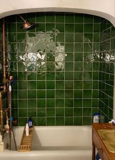 a bathtub with green tiles and wooden flooring next to a sink in a bathroom