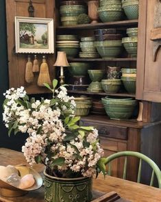 a wooden table topped with lots of plates and vases next to a shelf filled with bowls