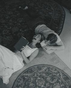 two people laying on the floor next to each other with a book in their hands