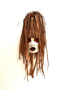 a white mask with long brown hair and sunglasses on it's face is hanging from the wall