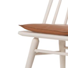 a white chair with a brown pillow on it's seat and the backrest