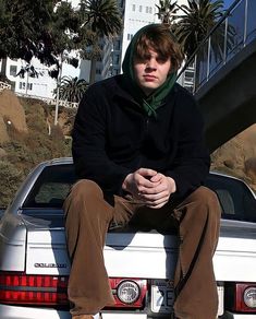 a young man sitting on the back of a white car in front of a building