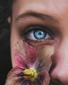 a woman with blue eyes holding a flower in front of her face