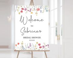 a welcome sign is on an easel in front of a white wall with flowers