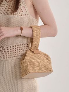 a woman in a beige dress holding a straw bag with her hand on the shoulder