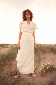 a woman standing in the sand wearing a white dress with ruffles on it