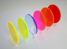 five different colored discs are lined up in a row on a white surface, with one being tilted to the side