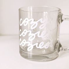 a clear glass mug with white writing on it