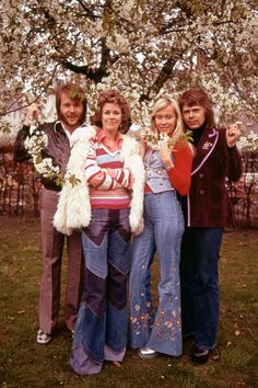 three women standing next to each other in front of a tree with flowers on it