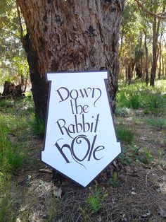 a sign that says down the rabbit hole next to a tree