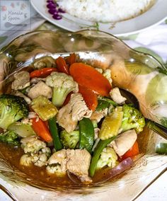 a bowl filled with meat and vegetables on top of a table next to white rice