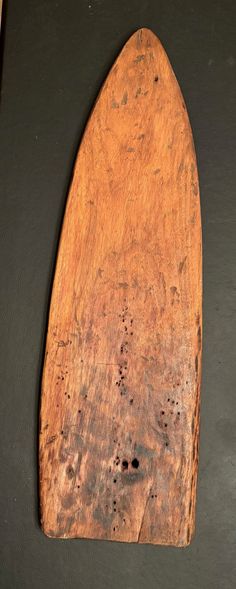 a wooden surfboard laying on top of a black table next to a brown wall