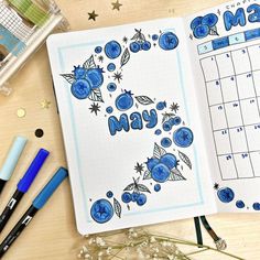 an open planner with blue flowers on it next to markers and pens, along with other office supplies