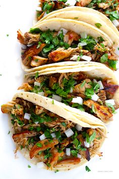 three tacos with chicken, cilantro and parsley on a white plate