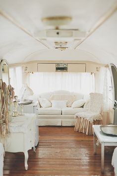 the inside of a camper with white furniture and mirrors on the wall, along with wood flooring