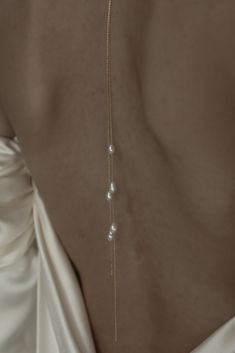 the back of a woman wearing a white dress with pearls on it's neck