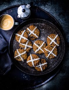 some cookies are on a black plate with icing and a cup of coffee next to it