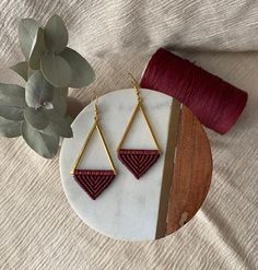 a pair of earrings sitting on top of a white plate next to a plant and yarn