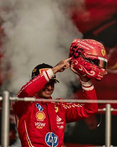 a man in a red racing suit holds his helmet over his head