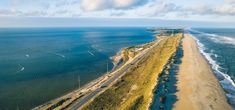 an aerial view of the beach and ocean with cars driving on the road next to it