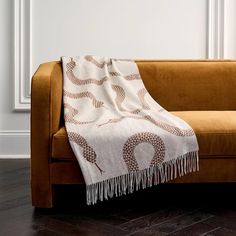 a couch with a blanket on it in front of a white wall and wooden floor