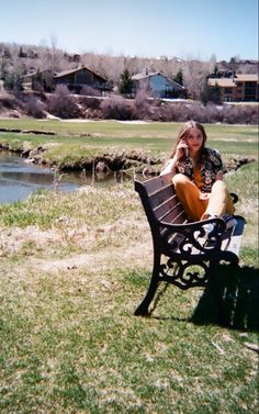 a woman sitting on top of a bench next to a river