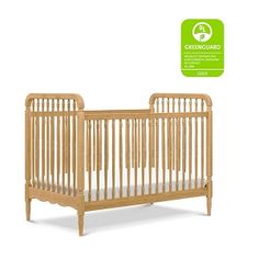 the crib is made from wood and has white sheets on it, as well as a green sticker