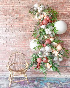 an artificial christmas tree made out of balloons and greenery is displayed in front of a brick wall