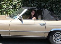 a woman sitting in the driver's seat of a tan convertible car, smiling