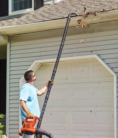 a man with a chainsaw in front of a garage holding onto the side of a house