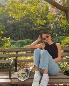 a woman sitting on top of a wooden bench next to a flower pot and sunglasses