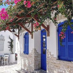 an outdoor patio with blue shutters and pink flowers on the wall, next to a white building