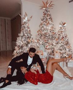 a man and woman laying on the floor next to a christmas tree