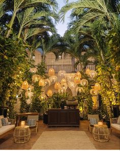 an indoor area with palm trees and lights hanging from it's ceiling, surrounded by wicker furniture