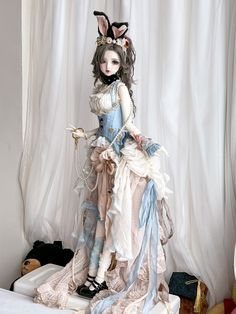 a doll is sitting on a bed in a room with white walls and curtains behind it