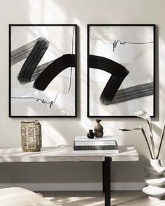 two black and white paintings hanging on the wall above a table in a living room